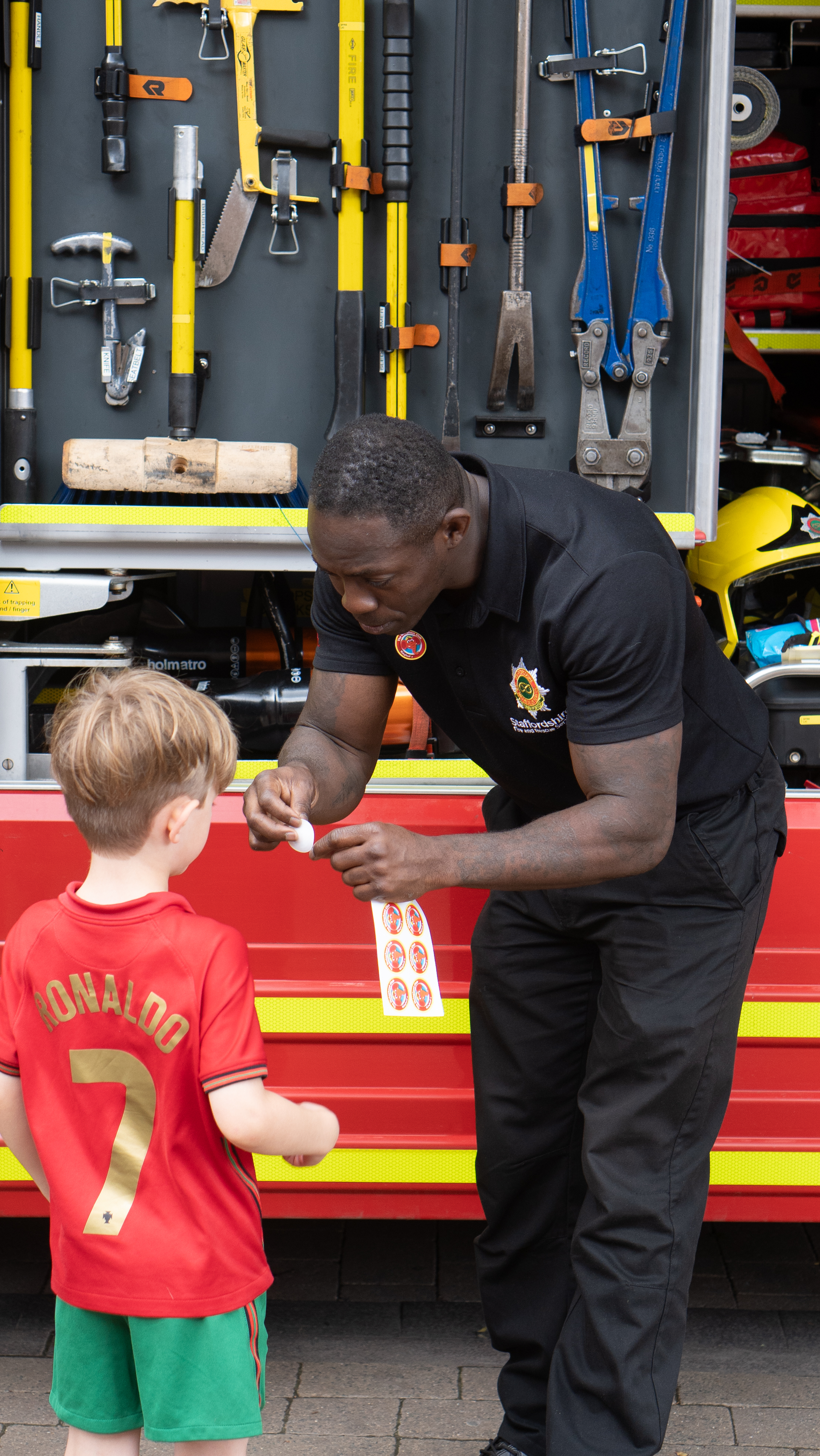 Firefighter giving a Welephant club sticker to a young boy at a community event.